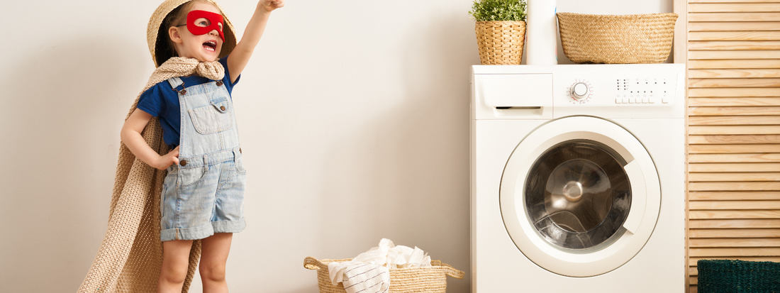 Child in a superhero cape reaching for the sky in front of the washing machine