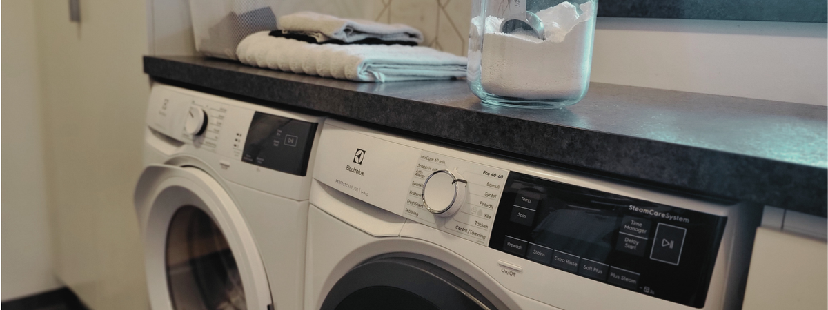 Washing machine and tumble dryer in the laundry room, with detergent in a glass jar and folded towels.