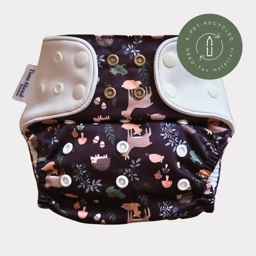 En mörklila tygblöja med ett whimsiskt mönster av rosa och bruna skogsdjur, svampar och löv på sin yttre yta.