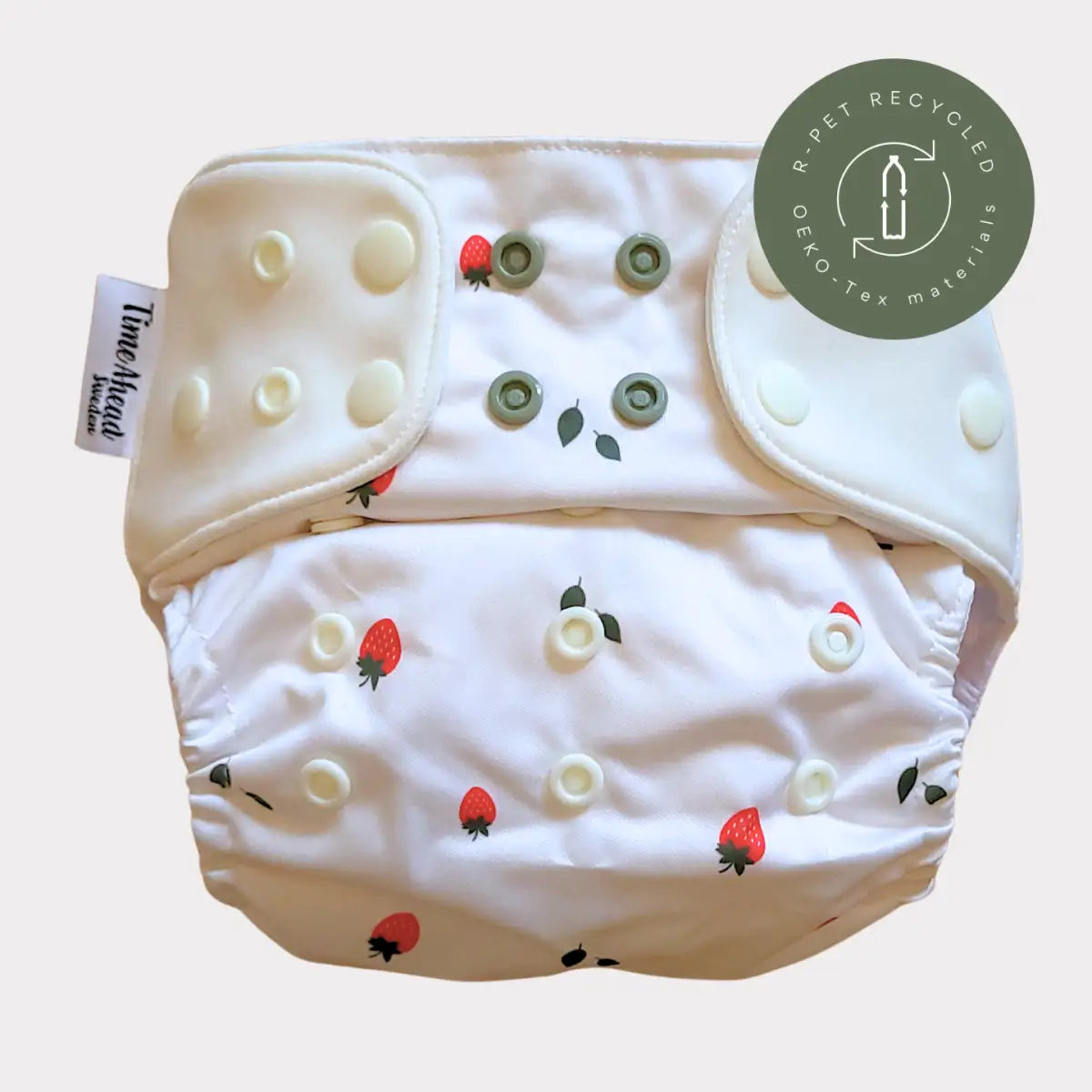 Vit återanvändbar tygblöja med jordgubbs- och bladtryck, med tryckknappar i krämigt och olivgrönt.