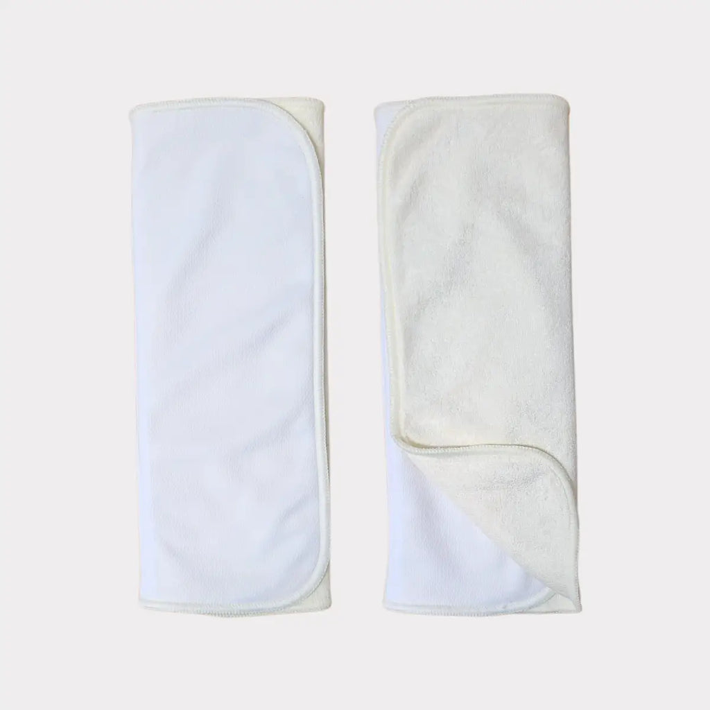 Två vita, mjukt texturerade tygblöjinlägg med en subtil ribbad kant och prydligt vikta hörn.