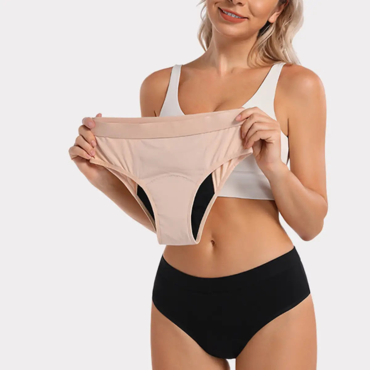 En kvinna håller upp ett par beigea periodkalsonger över sina svarta kalsonger.