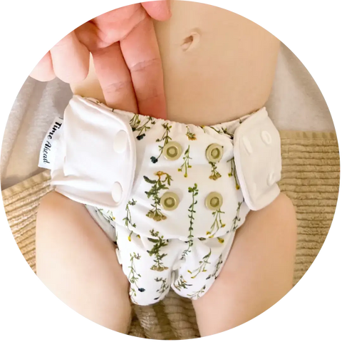 Baby i vit tygblöja med grönt och gult blommönster, passar bäst som onesize tygblöja