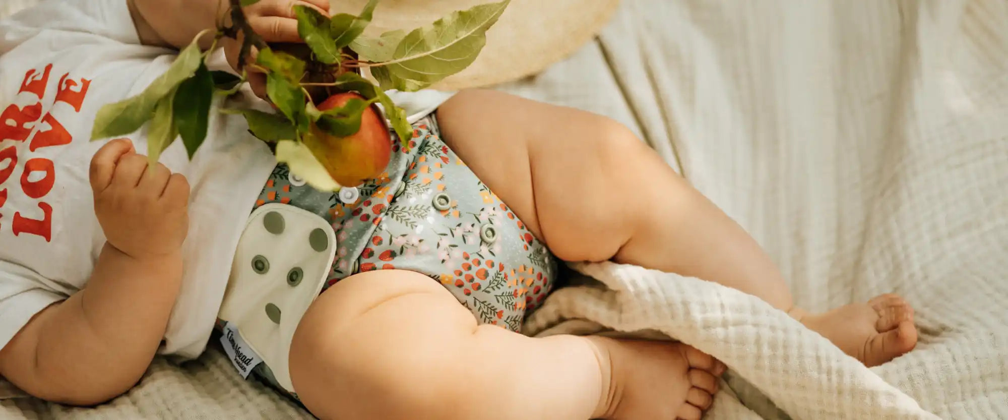 Baby i en blommönstrad tygblöja som håller en äppelgren.
