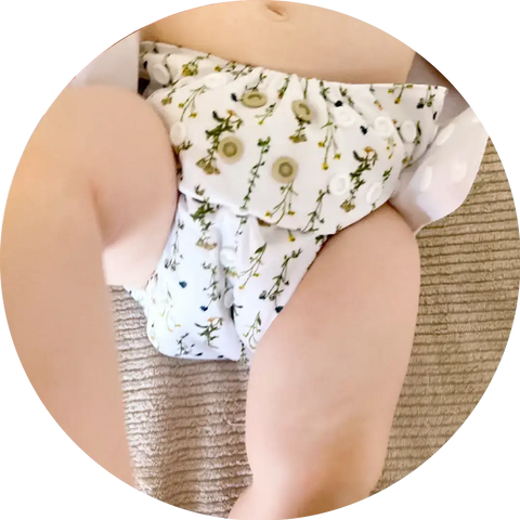 Babytjej i vit tygblöja med grönt blommönster, passar bäst som onesize tygblöja