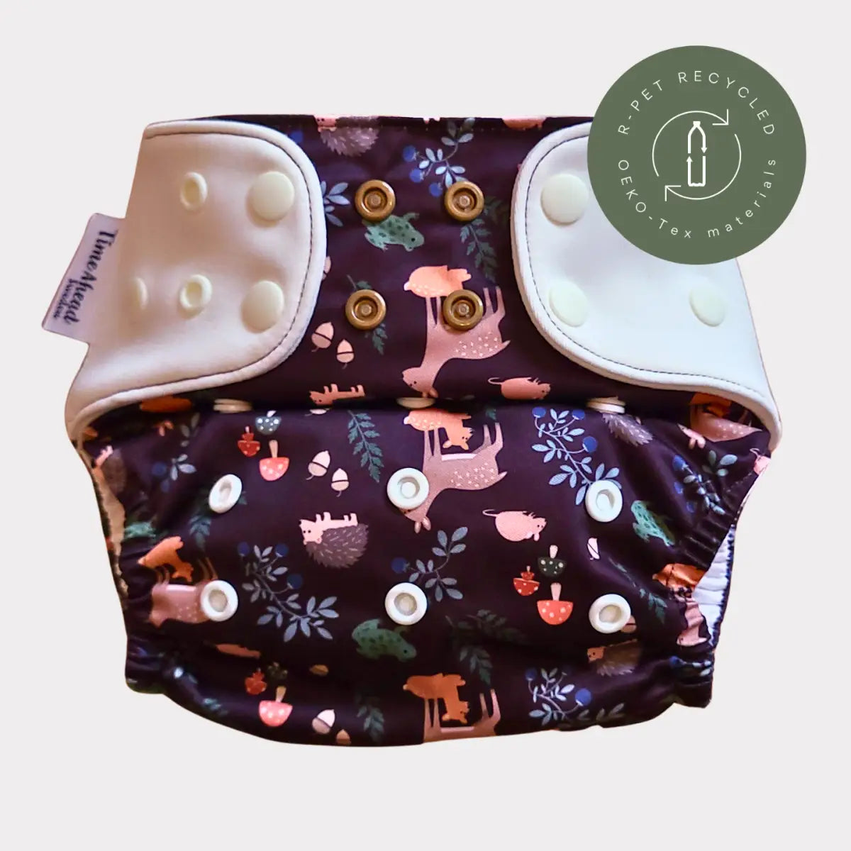 En mörk lila återanvändbar tygblöja med ett lunnefullt skogsdjurstryck som visar rosa, bruna och gröna varelser bland bladverk.