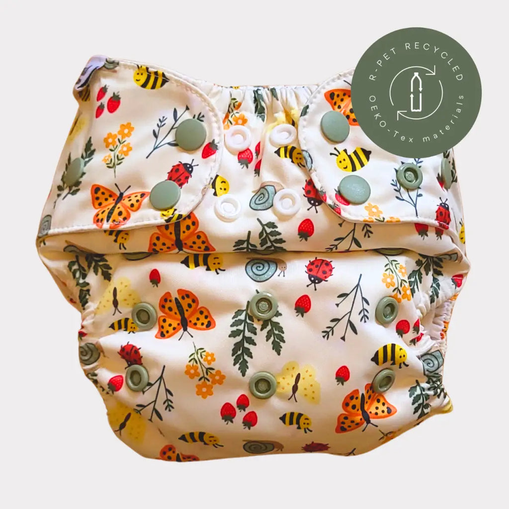 En lekfull, krämfärgad tygblöja med ett lekfullt mönster av orange fjärilar, gula bin, röda nyckelpigor och jordgubbar på ett mjukt tyg med gröna tryckknappar.