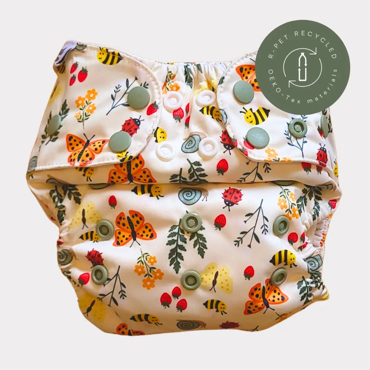 En lekfull, krämfärgad tygblöja med ett lekfullt mönster av orange fjärilar, gula bin, röda nyckelpigor och jordgubbar på ett mjukt tyg med gröna tryckknappar.