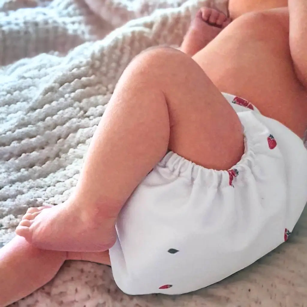 En bebis med en vit tygblöja med jordgubbsmönster.