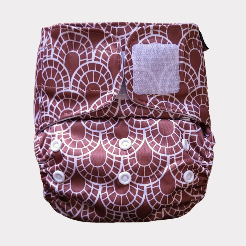 En mörkröd och vit mönstrad tygblöja med vågformad design, med vita tryckknappar och en kardborre-flap.