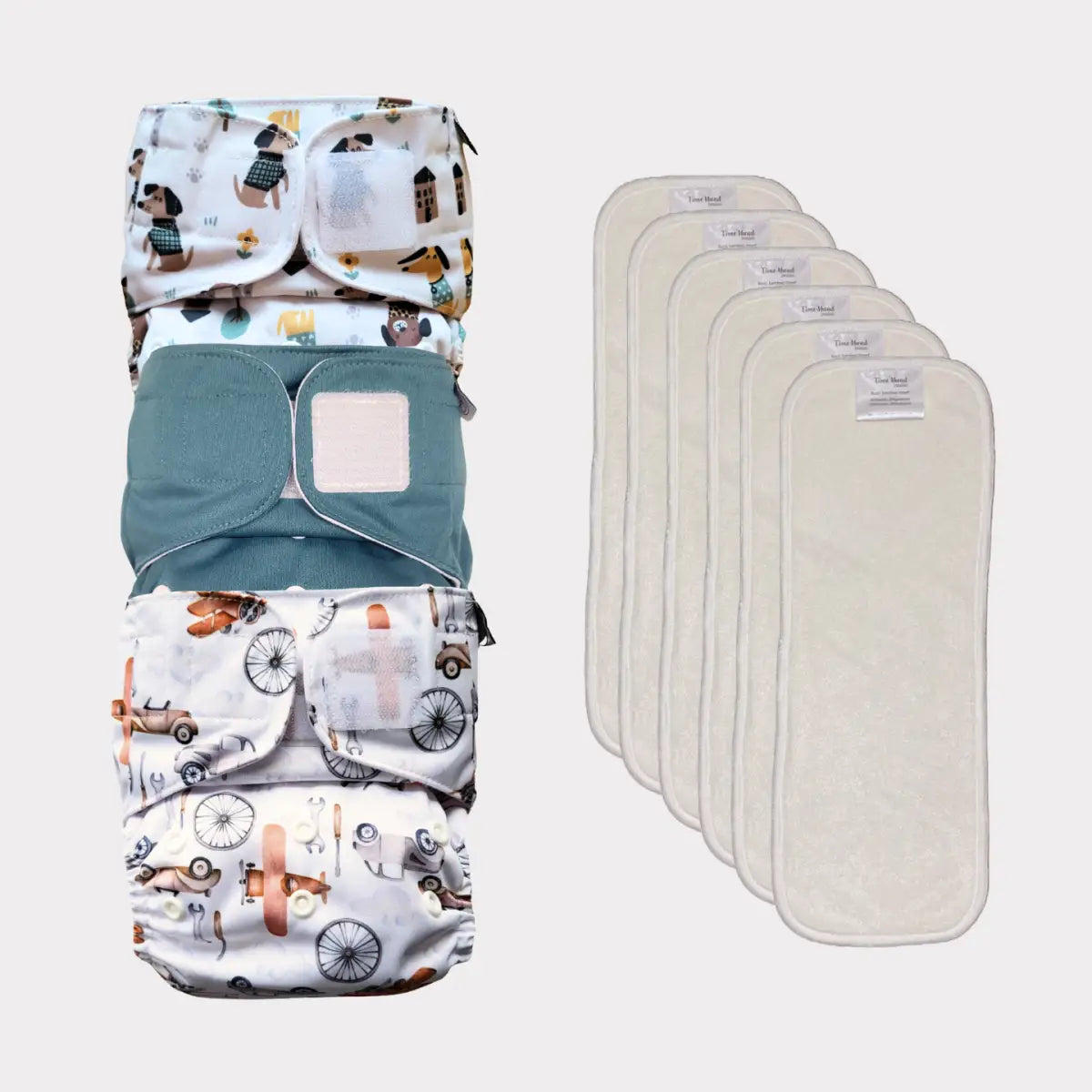 Staplad återanvändbara tygblöjor med lekfulla djur- och fordonstryck i vita, turkosa och krämfärgade tyger.