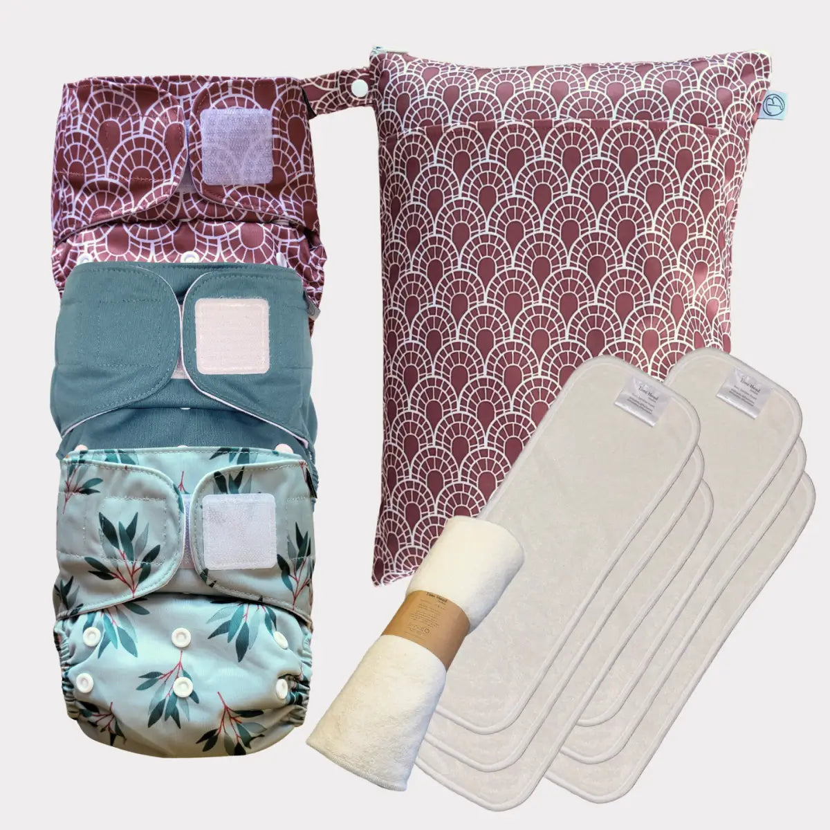 Ett set med tre tygblöjor i mjuka pastellfärger med blad- och geometriska mönster, tillsammans med en matchande mönstrad förvaringsväska och vita absorberande inlägg.