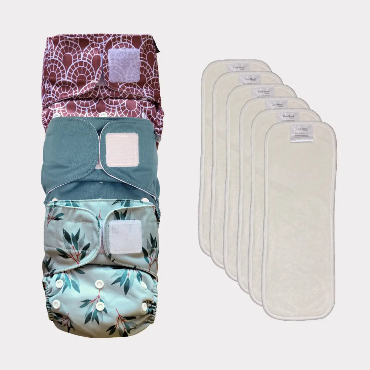 Sats av fyra mönstrade tygblöjor med tryckknäppningar och matchande vita inlägg, tillsammans med sex enkla beige återanvändbara blöjinsatser.