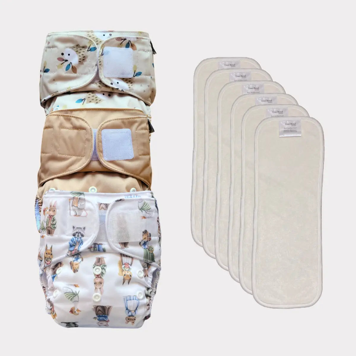 Tre återanvändbara tygblöjor med söta djurtryck och tryckknäppningar, tillsammans med sex matchande absorberande inlägg.