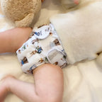 Baby med vit tygblöja med ett finurligt mönster av små figurer och föremål.