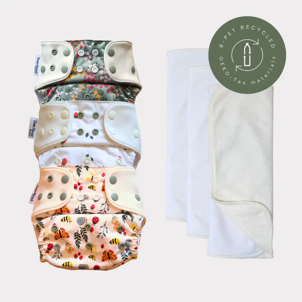 Staplat miljövänliga tygblöjor med blommönster och insektsmönster i mjuka pastelltoner, med tryckknäppningar och ett vitt absorberande insats.
