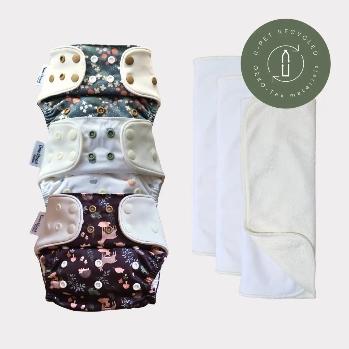 Tre återanvändbara tygblöjor med blommiga och djurtryck, med tryckknäppningar i kräm eller beige toner.