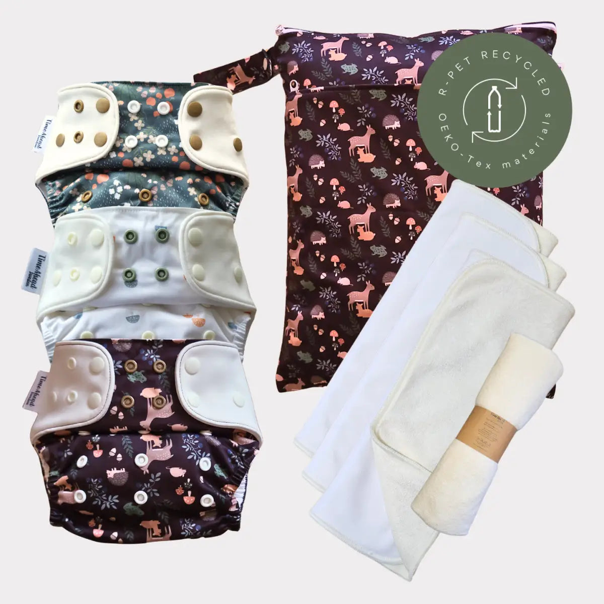 Sats av tre återanvändbara tygblöjor med skogsdjurstampar och tryckknäppningar, tillsammans med en matchande förvaringsväska tillverkad av återvunna material.