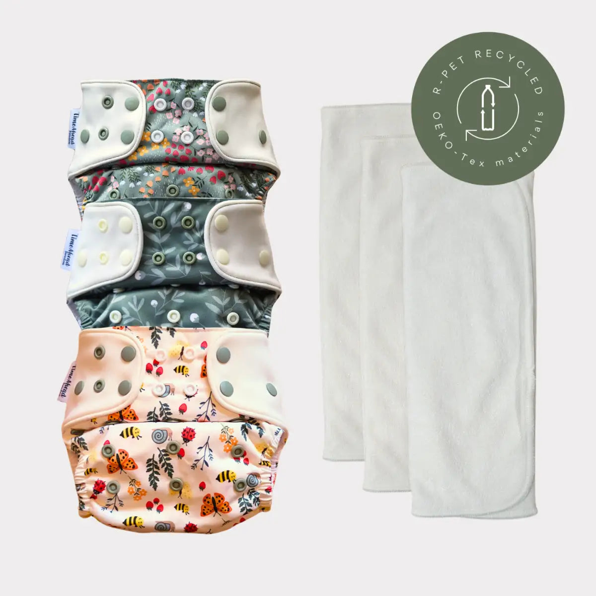 En stapel med fyra färgglada, mönstrade tygblöjor med blommor- och insektsdesigner, med vita tryckknäppningar och mjuk tyg.