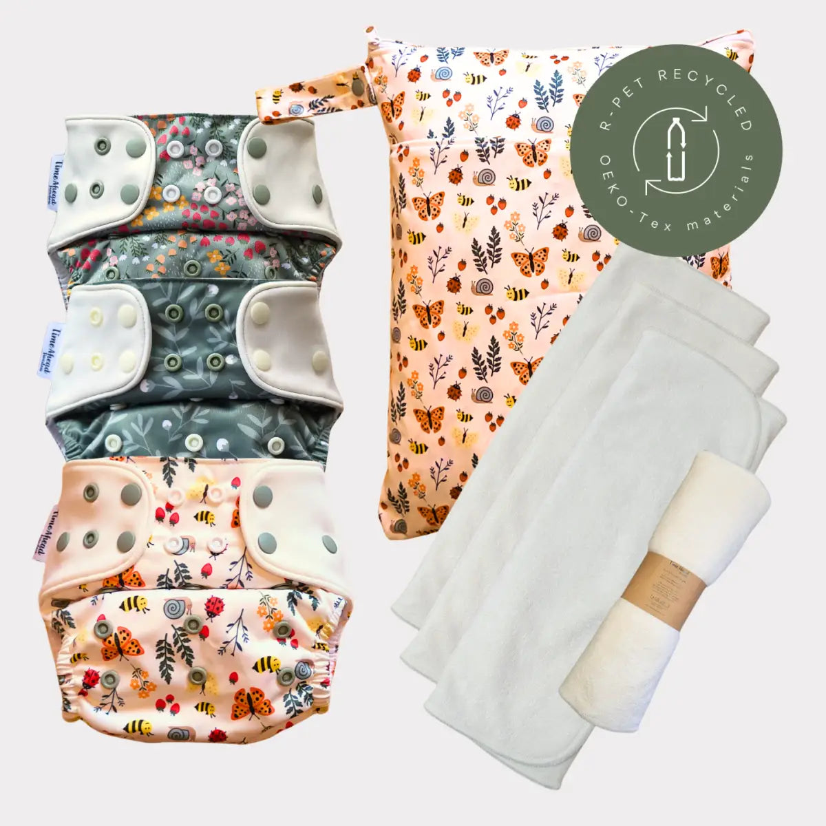 Sats av tre återanvändbara tygblöjor med blommönster och insektsmönster i mjuka pastelltoner, med tryckknäppningar och en matchande mönstrad blöjväska tillverkad av återvunna oeko-tex-material.