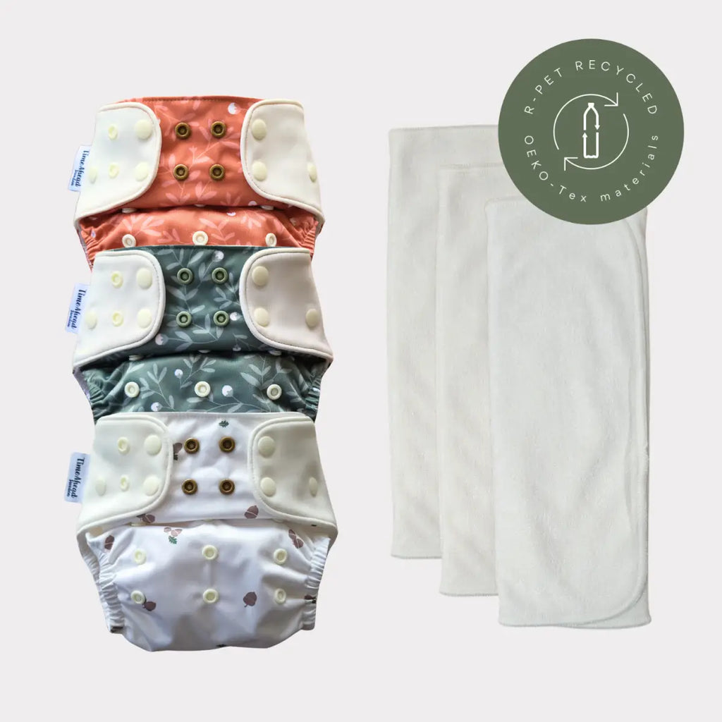 En bunt med fyra återanvändbara tygblöjor med tre vita absorberande inlägg, tillverkade av återvunna, Oeko-Tex-certifierade material.