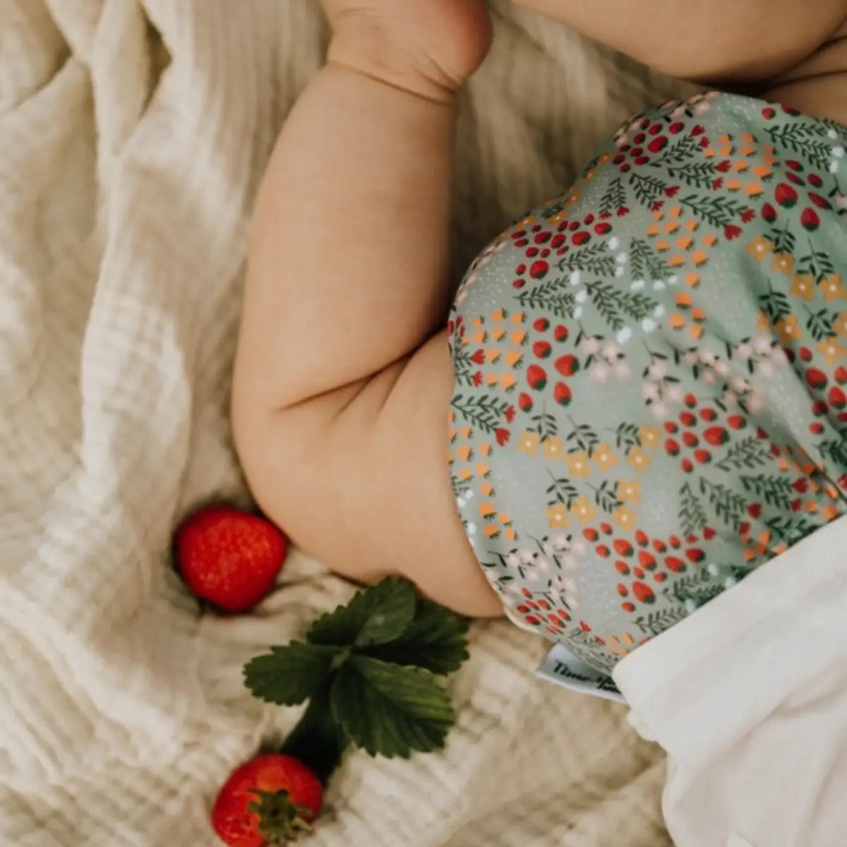 En mjuk ljusgrön pocketblöja i återvunnet material med mönster av röda jordgubbar och gula blommor i startpaket komfort