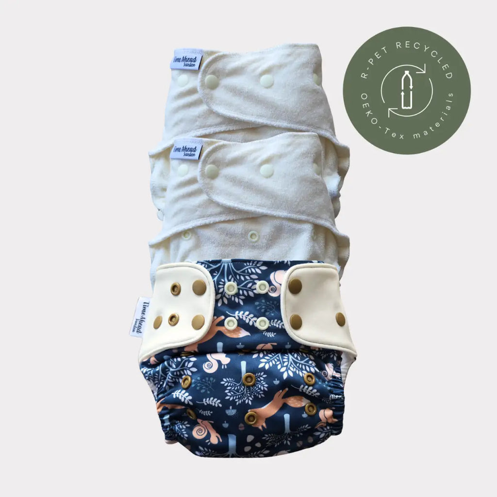 Stapel med fyra tygblöjor, tre vita och en mörkblå med mönster av skogsdjur.