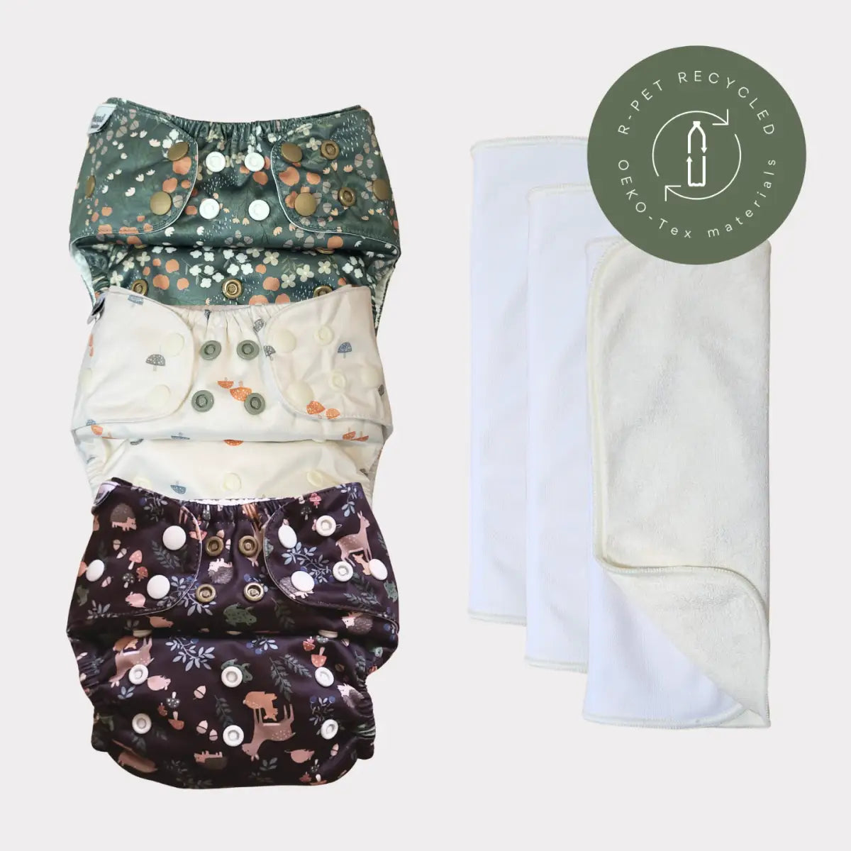 Tre återanvändbara tygblöjor med blommönster i grönt, kräm och mörk lila, var och en med knäppningsstängningar.