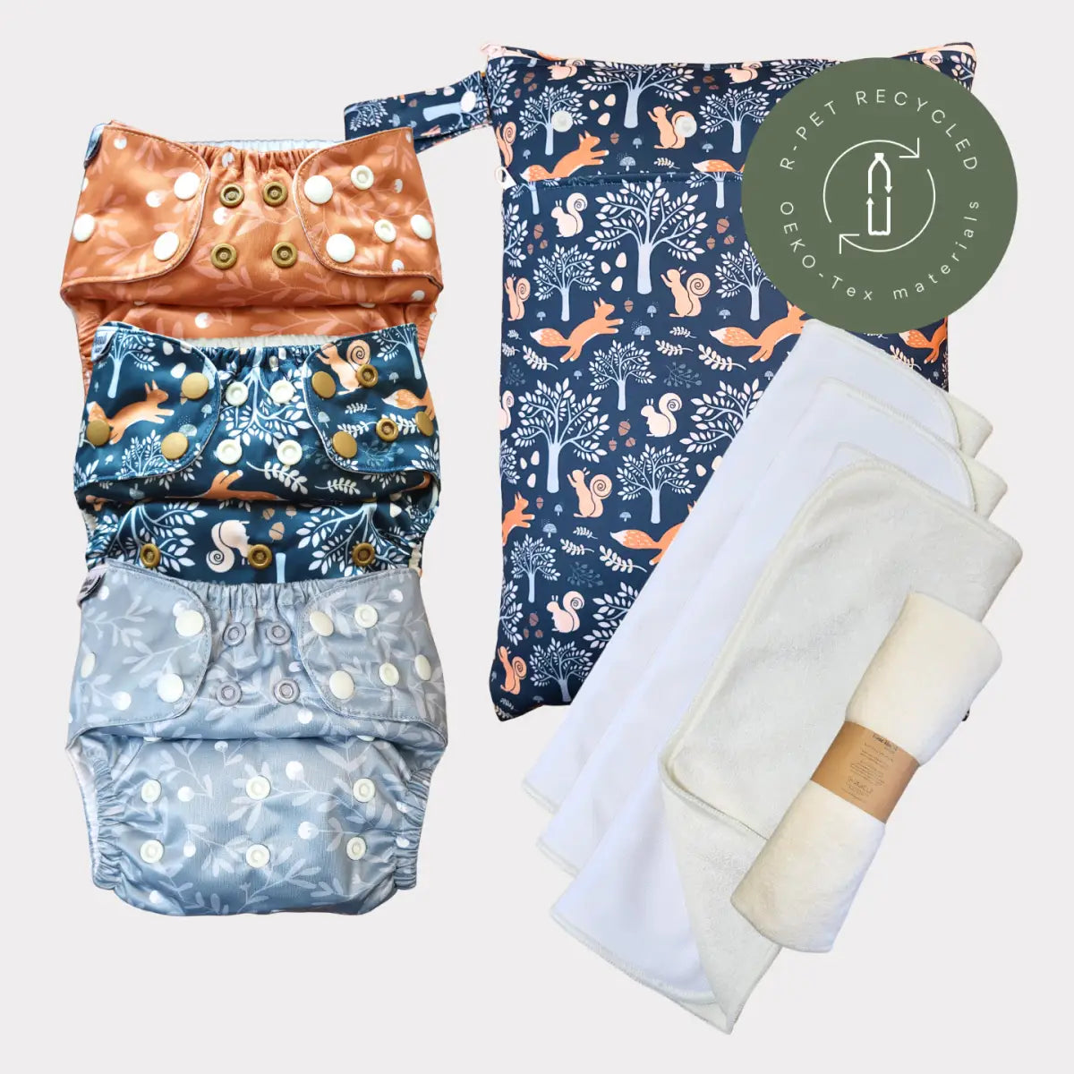 Sats av tre återanvändbara tygblöjor med skogsdjurstryck i orange, marinblått och ljusgrått, med knäppningsstängningar och en matchande mönstrad förvaringsväska.