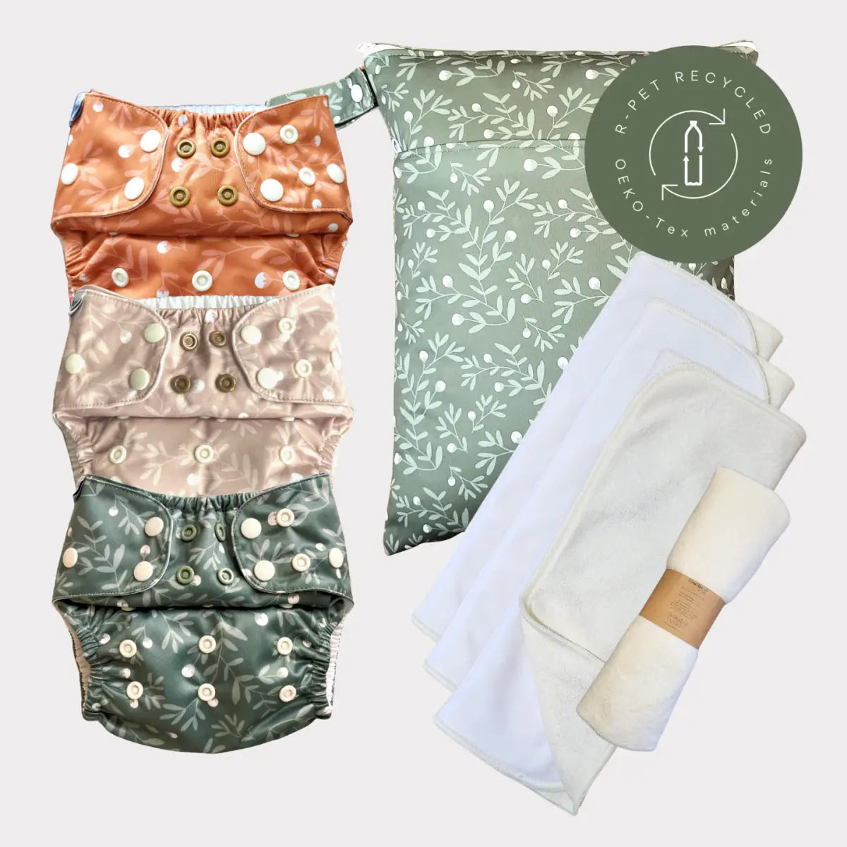 Sats med tre återanvändbara tygblöjor i jordnära toner med bladmönster och knäppningsknappar, tillsammans med en matchande förvaringsväska.