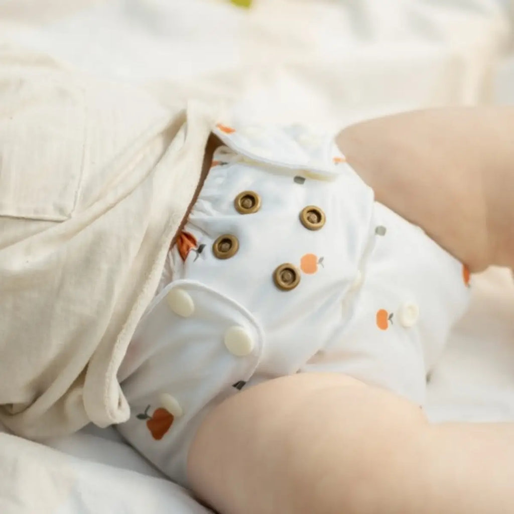 Tygblöja slim blöjskal med vita tygblöjor och orange fruktmönster samt bruna och vita tryckknappar