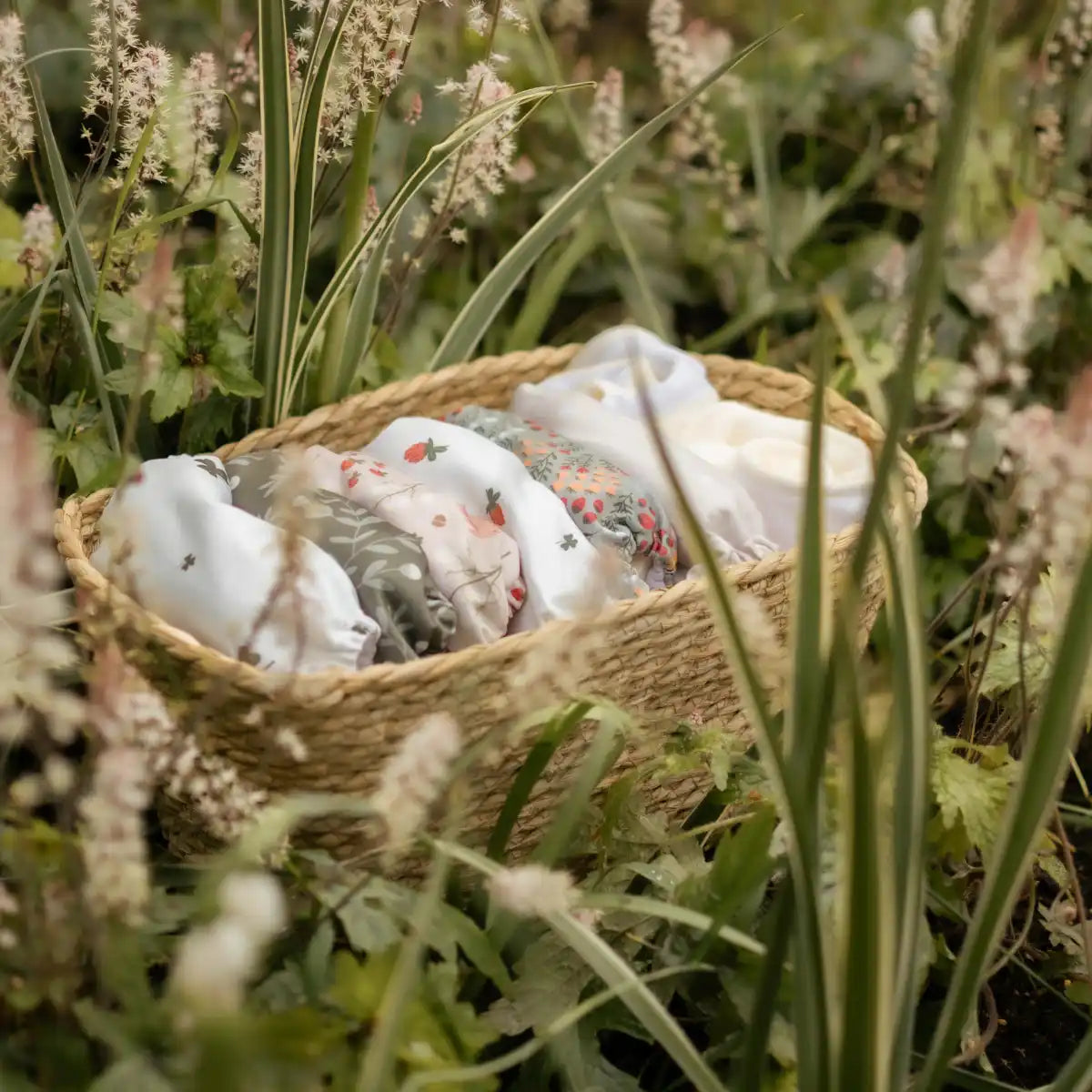 En vävd korg fylld med vikta babykläder i olika mönster.