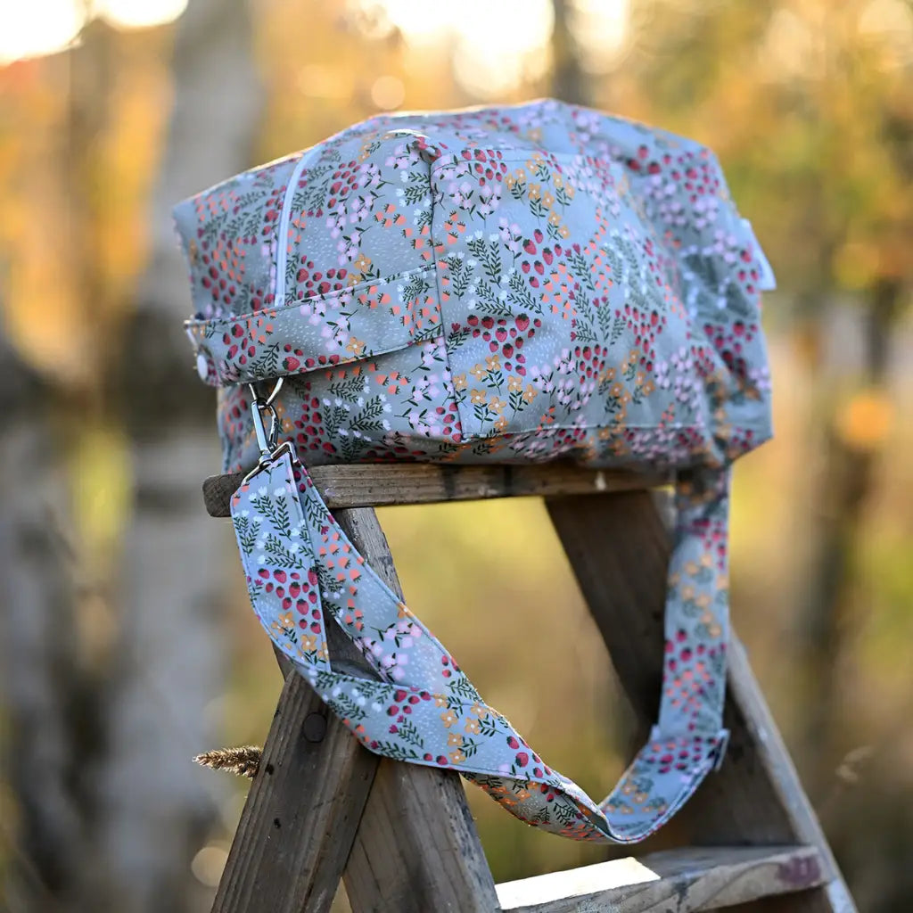 Ljusblå duffelväska med blommigt tryck och avtagbar axelrem.